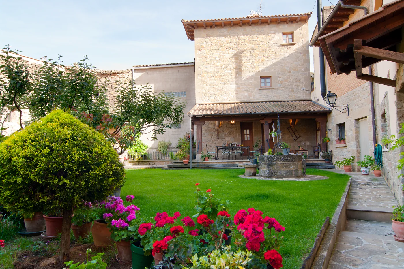 Jardín con pozo y porche junto a la fachada de piedra de Casa Rural El Pajar