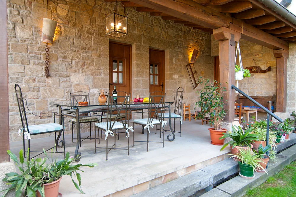 Porche cubierto con mesa, sillas y plantas junto al jardín
